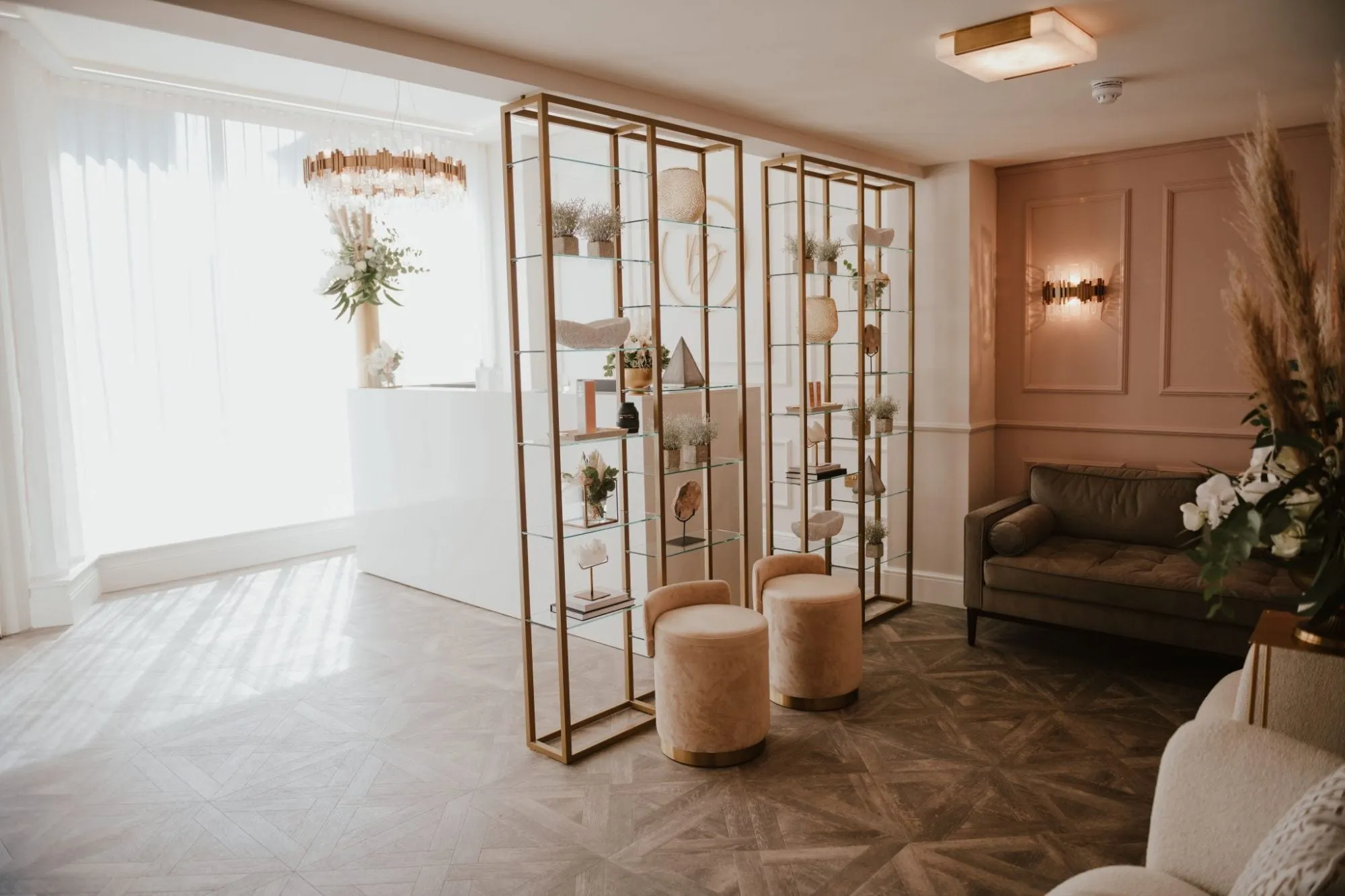 Reception with brass display shelving, chandelier and blush velvet stools at Blossom Cosmetic Clinic, York